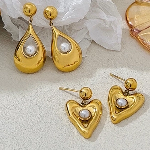 Detailed shot of gold irregular earrings with white pearls on a minimalist textured surface