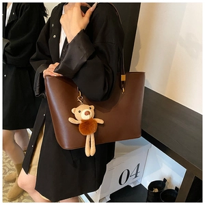 Detail of dark brown leather tote bag with a knitted bear charm and gold ring hardware