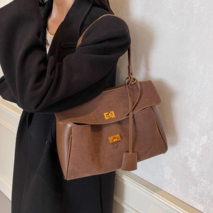 Sac fourre-tout en daim marron avec fermoirs dorés porté sur un manteau de mannequin