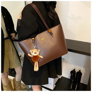 Close-up of brown leather tote bag with gold logo and plush bear charm accessory