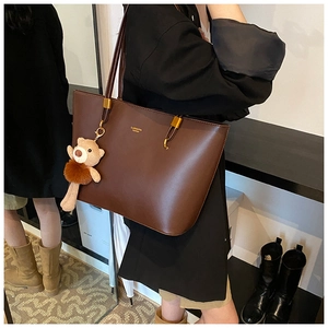 Detail of a dark brown leather tote bag with a plush bear charm and thin shoulder strap