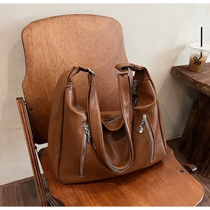 Macro detail of retro brown PU leather tote bag with vertical zippers on a wooden chair