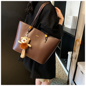 Detail view of brown leather tote bag with slim straps and a cute teddy bear charm