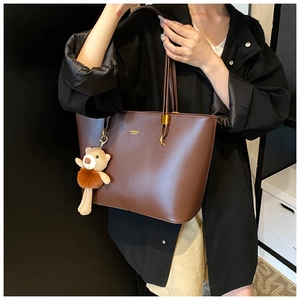 Detail of coffee brown leather tote bag featuring gold logo and cute plush bear charm