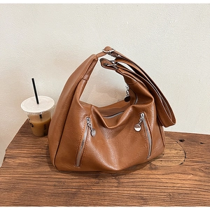 Detail view of brown pebbled faux leather hobo bag on a rustic wooden bench with coffee