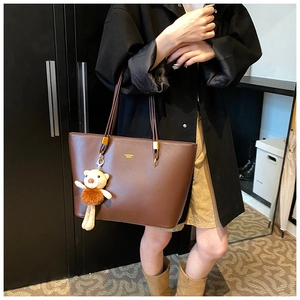 Detail of dark brown leather tote bag with bear charm and golden logo on shoulder