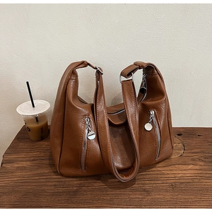 Close-up of brown faux leather tote bag with dual vertical zippers on a wooden table
