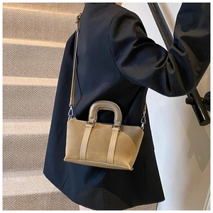 Close-up of khaki frosted leather handbag held by model in a minimalist staircase setting