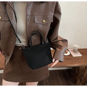 Détail d'un sac seau en toile noire porté avec une veste en cuir au style vintage chic