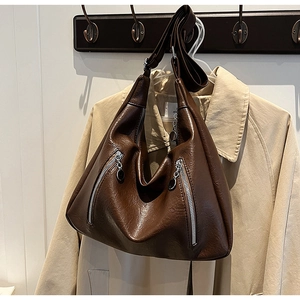 Detail of dark brown leather tote featuring silver zippers and textured pebbled finish