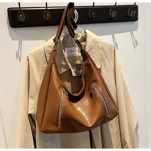 Detail of caramel leather hobo bag with dual metal zippers hanging over a beige trench coat