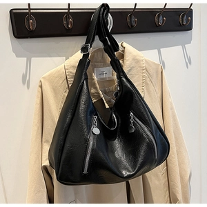 Detail of black leather tote bag with silver zippers styled on a khaki trench coat