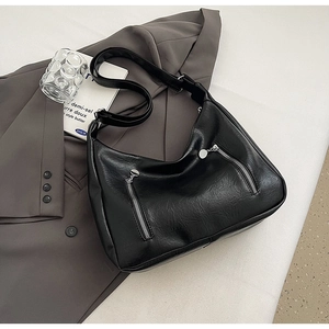 Detail of black vintage leather tote bag with silver zippers on a grey suit background