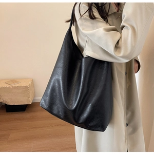 Close-up of a large black textured leather tote bag worn as a shoulder bag on a model