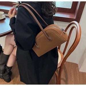 Brown suede boston bag shown from a side view on a model in a cafe setting