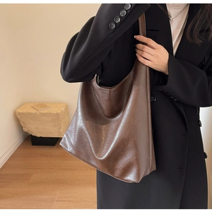 Detail of dark brown tote bag in vintage faux leather texture worn with a black suit
