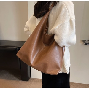 Side view of a brown large capacity PU leather tote bag worn by a model on shoulder