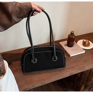 Detailed view of a black canvas shoulder bag with white stitching on a wooden surface
