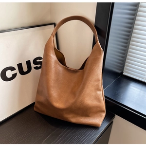 Close-up of brown textured PU leather tote bag with wide shoulder strap and soft silhouette