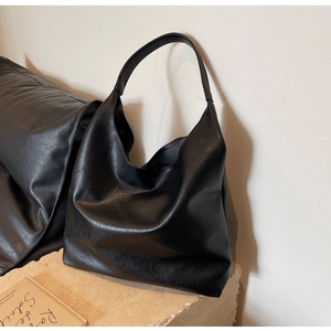 Detail of a minimalist black PU leather hobo bag with textured finish on a stone base