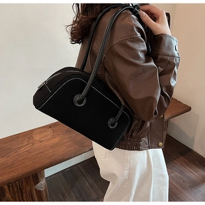 Detail of a black suede Boston bag with white stitching shown on a model's shoulder