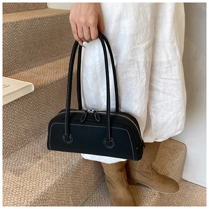 Detail of a black minimalist tote with white contrast stitching and slim shoulder straps