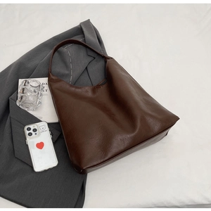 Detail of dark brown matte faux leather tote bag laid over a grey suit jacket
