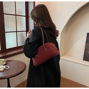 Deep red suede Boston bag worn on shoulder by model in a cozy indoor setting