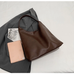 Flat lay of a large brown PU leather tote bag with office accessories and blazer