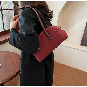 Detailed side view of a dark red suede Boston shoulder bag worn by a model in a room
