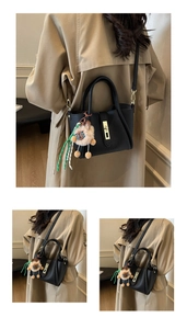 Close-up of black litchi grain leather bucket bag with gold hardware and plush sheep charm
