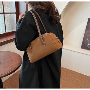 Brown suede shoulder bag with contrast stitching shown on a model in a warm interior