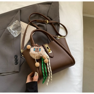 Detail of dark brown pebble leather handbag with gold lock and plush animal charm