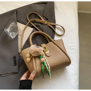 Close-up of brown lychee leather bucket bag with gold clasp and plush ball accessory