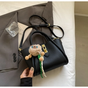 Detail of black pebbled leather bucket bag with gold hardware and plush clown charm