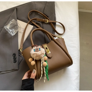 Close-up of brown litchi pattern leather bucket bag with gold clasp and plush charm