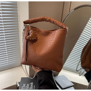 Détail du sac seau marron tressé avec poignée froncée et breloque en forme de cœur argenté