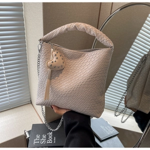Détail du sac seau tressé beige avec bandoulière chaîne et breloque coeur sous lumière douce