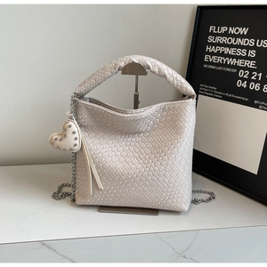 Détail du sac seau en cuir tressé beige avec charm cœur à clous et bandoulière chaîne