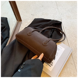 Detail of chocolate tote bag with contrast stitching on elegant black coat and magazine
