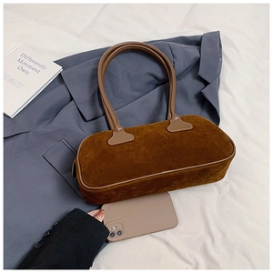 Detailed view of the caramel brown suede bowling bag next to a smartphone for size scale