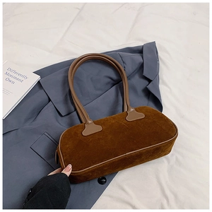 Close-up of brown suede bowling bag with leather handles on a navy blazer backdrop