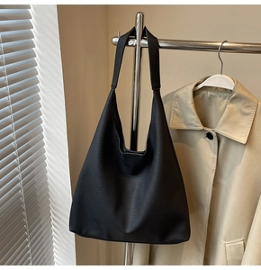 Detail of minimalist black leather tote bag with lychee texture hanging on chrome rack