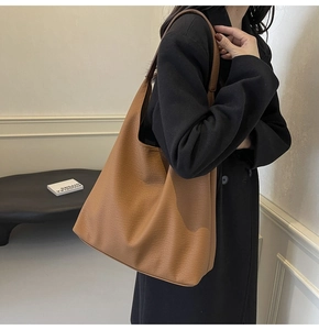 Brown litchi leather tote bag shown on shoulder in minimalist interior scene