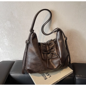 Detail of coffee brown leather tote bag with bow tie accent and metallic magnetic buckle