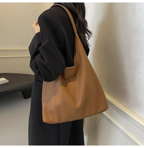 Close-up of a large caramel tote bag in pebble leather worn with a black blazer