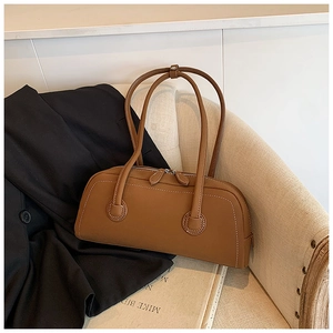 Detail view of brown leather tote bag with white contrast stitching on a cream sofa