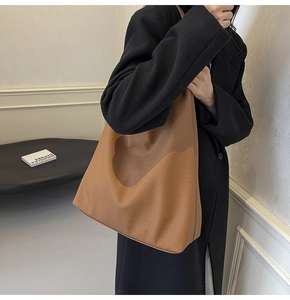Detail of the large caramel pebble leather hobo bag worn by a model in a minimalist room