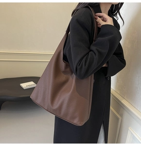 Close-up of a large brown leather tote bag with lychee texture worn with a black coat