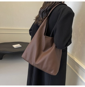 Brown leather tote bag featuring a textured finish shown as worn by a model in minimalist room